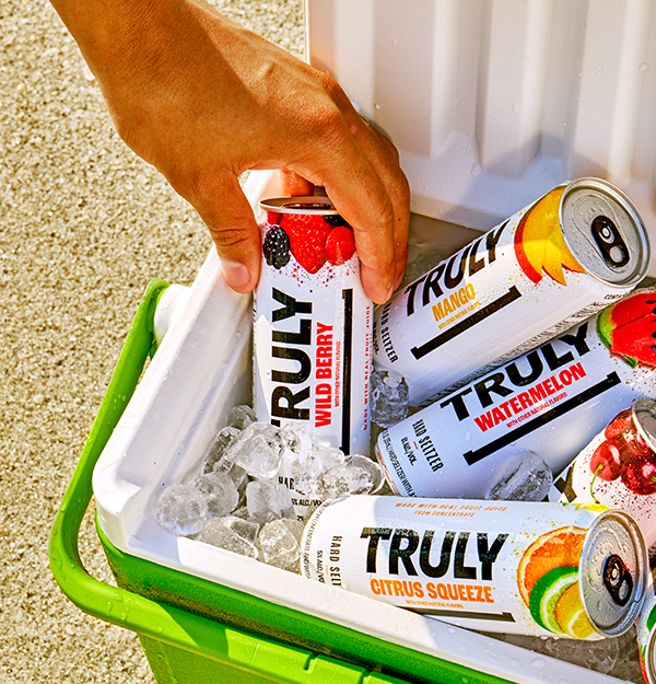 Cooler of Truly Cans in ice with a hand grabbing one