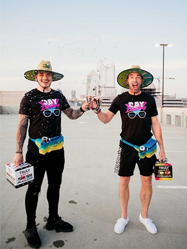 Two Men holding packs of Truly Hard Seltzer and cheers-ing